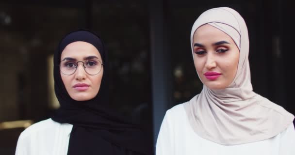 Close-up portret van twee jonge Arabische mooie vrouwen in traditionele hoofddoek en bril kijken naar de camera. Behoorlijk vrolijke moslimvrouwen in hijab op straat. Islamitische charmante gelukkige dames — Stockvideo