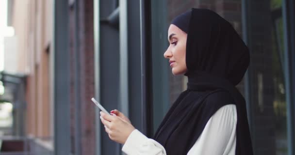 Primer plano retrato de mujer árabe en pañuelos tradicionales mirando el teléfono y sonriendo. Bastante musulmana hembra en hijabs leer mensajes, mensajes de texto, navegar por Internet en el teléfono inteligente después de ir de compras. — Vídeos de Stock