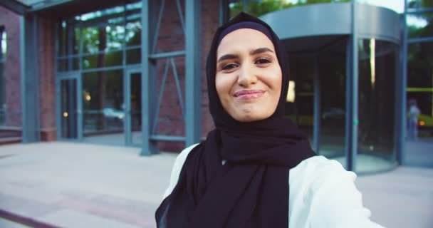POV młodej muzułmańskiej pięknej kobiety w tradycyjnej chustce stojącej na zewnątrz i rozmawiającej przez kamerę internetową. Koncepcja Videochat. Ładna kobieta z zakrytą głową machająca ręką do kamery i wideo. — Wideo stockowe