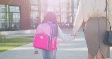 Annesiyle okula giden pembe sırt çantalı, beyaz, neşeli, küçük bir kız. Güzel, küçük bir kız öğrenci okula iyi bir ruh halinde koşuyor. Okula dönelim. Aile kavramı