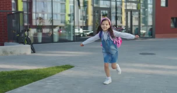 Καυκάσιος χαρούμενη χαριτωμένο κοριτσάκι με ροζ σακίδιο τρέχει στην αυλή του σχολείου μετά τα μαθήματα και χαμογελώντας. Όμορφη χαρούμενη μικρή νεαρή μαθήτρια που φεύγει από το σχολείο με καλή διάθεση. Έννοια συναισθημάτων — Αρχείο Βίντεο