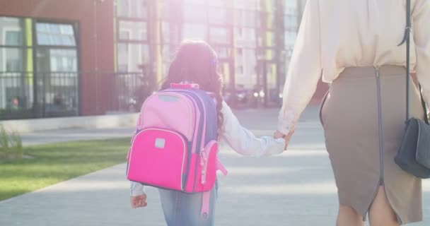 Traseira de caucasiano alegre menina bonito com mochila rosa indo com a mãe para a escola. Linda pequena estudante júnior do sexo feminino correndo para a escola de bom humor. De volta à escola. Conceito familiar — Vídeo de Stock