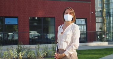 Güneşli bir günde karantinada okul bahçesinde maske takmış neşeli güzel bir kadının portresi. Kasabada caddede keyifli beyaz bir kadın var. Okulun yanında bekleyen insanlar