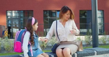 Okulun yanındaki bankta oturan beyaz bir kadının portresi. Küçük tatlı bir kız öğrenci açık havada sohbet ediyor. Mutlu güzel anne kızına sarılıyor ve kahvaltıdan önce ona bir paket veriyor..
