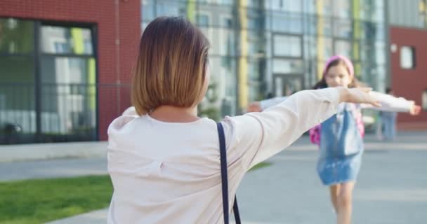 Traseira de mulher caucasiana à espera de uma filha bonita estudante júnior na frente da escola depois das aulas. Retrato de colegial feliz com mochila rosa correndo para a mãe e abraçando. Conceito do estudo — Vídeo de Stock