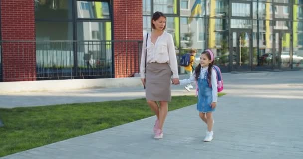 Кавказька вродлива жінка ходить з маленькою молодшою донькою на вулиці і розмовляє в сонячний день. Радісна жінка ходить зі своєю дівчиною зі школи і розмовляє в доброму гуморі. Сімейна концепція — стокове відео