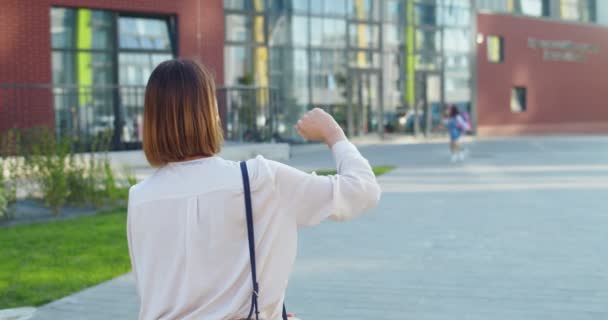 Visão traseira da mulher bonita caucasiana encontrando colegial bonito pouco da escola depois das aulas. Feche-se de aluno de criança alegre com mochila rosa correndo para a mãe e abraçando-a. Conceito familiar — Vídeo de Stock