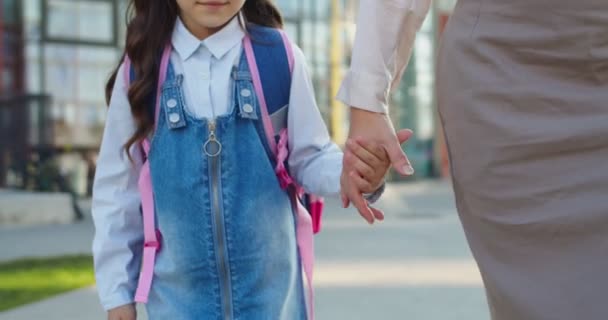 Beyaz bir kadın sırt çantalı küçük bir kızın elini tutuyor ve açık havada okula gidiyor. Anneye yakın olmak, kız öğrenciyi derslere götürür. Okula dönelim. Öğrenci konsepti — Stok video