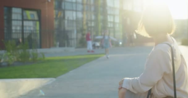 Güneşli bir günde küçük bir öğrenciyle tanışan beyaz, neşeli, güzel bir kadının portresi. Dersten sonra annesine koşan ve dışarıda kucaklaşan küçük, mutlu bir kız öğrenci. Çocuk eğitimi konsepti — Stok video