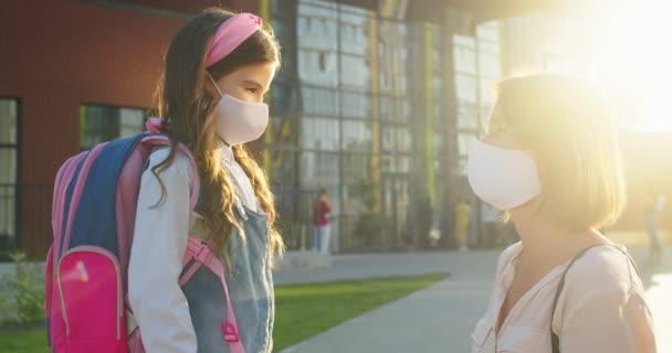 밝은 날 학교 밖에서 카메라를 보고 있는 백인 여성과 마스크를 쓴 어린 여학생의 초상화. 격리되어 있는 기분이 좋은 아름다운 엄마와 딸. 닫기 개념 — 비디오