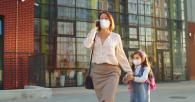 Güneşli bir günde okuldan tatlı bir kızla yürürken maske takmış, akıllı telefondan konuşan beyaz bir kadın. Cep telefonu okul konseptinden arayan küçük kız annesinin ilgisini çekmeye çalışıyor.