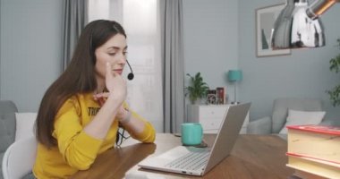 Kulaklıklı neşeli, güzel, beyaz bir bayanın evdeki laptopta görüntülü sohbet edişinin yan görüntüsü. Bilgisayarda görüntülü konuşma yapan mutlu bir kızın portresi. Video çağrısı kavramı