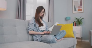 Evinde dizüstü bilgisayarla çalışan, gözlüklü, esmer, güzel, beyaz bir kız. Konsantre olmuş genç bir kadın rahat oda Freelance konseptiyle kanepede otururken bilgisayarda yazıp geziniyor.