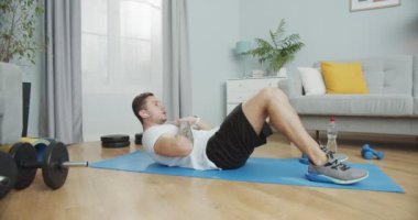 Sporcu adam antrenman yapıyor ve evde kulaklıkla müzik dinliyor. Erkek, ellerini göğsüne koyan bir paspasın üzerinde egzersiz yapıyor. Sağlıklı yaşam tarzının spor ve eğitim konsepti.