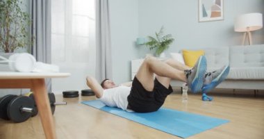Genç sporcu adam spor yapıyor, evde müzik dinliyor. Kaslı adam göğüs egzersizi yapıyor, gövdesini büküyor ve dizlerini büküyor, dirseklerini vücuduna geçiriyor. Sağlıklı ve zengin kavramı