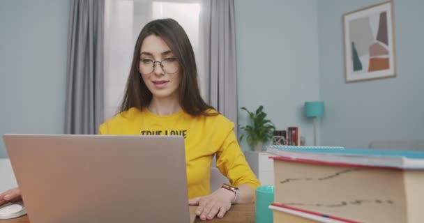 Gelukkig mooi meisje in bril opent laptop en zoeken internet terwijl zitten aan tafel thuis in goed humeur. Mooie blanke vrolijke vrouw browsen op de computer in gezellige kamer. Vrijetijdsconcept — Stockvideo