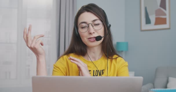 Jovem caucasiana bonita alegre no fone de ouvido falando em videocall no laptop no fone de ouvido em casa. Close up retrato de vídeo menina bonita feliz conversando no computador no quarto. Conceito de lazer — Vídeo de Stock