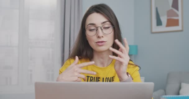 Närbild porträtt av koncentrerad söt flicka video chatta på datorn i rummet hemma. Vacker vit ung kvinna i glasögon med video konversation på laptop inomhus. Fritidsidé — Stockvideo