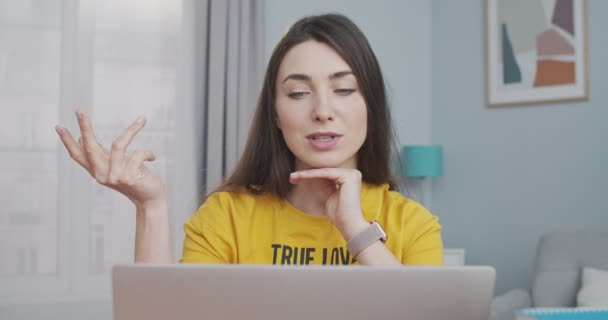 Primer plano retrato de chica bonita caucásica concentrada hablando en videollamada en la computadora en la habitación en casa. Hermosa joven morena mujer teniendo video conversación en el interior del ordenador portátil. Concepto de conversación — Vídeos de Stock