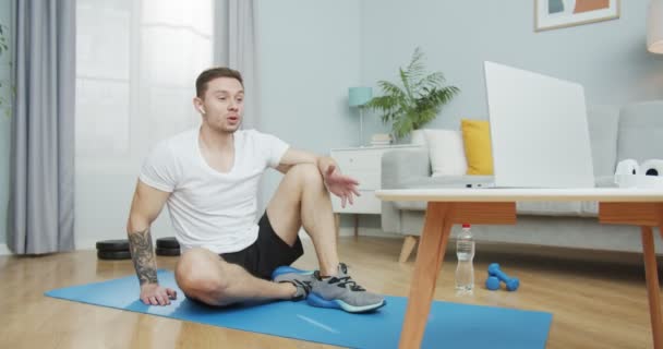 Um instrutor de fitness atlético falando em uma webcam labtop streaming aulas de treinamento online. Um desportista musculoso a falar com os seus seguidores sobre ginástica, atletismo. Exercício em casa, distância social. — Vídeo de Stock