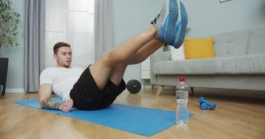 Kaslı bir adam evde nefes almayı kontrol ediyor. Sportif bir erkek karın kası egzersizi yapıyor, bacaklarını kaldırıyor, bir şişe su kullanıyor. İçeride, karantina sırasında evde eğitim, tecrit süresi.