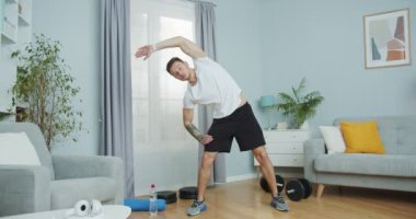 Beyaz tenli yakışıklı bir adam spor yapıyor, evde çalışıyor. Genç ve kaslı bir adam ısınıyor, yanlara doğru eğiliyor ve sağlıklı yaşam tarzının tadını çıkarıyor. Sağlık ve sağlık hizmetleri kavramı.