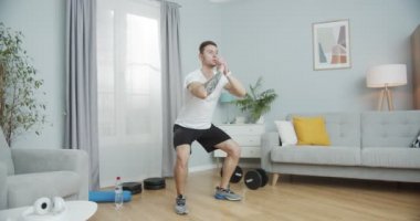 Spor yapan genç bir adam, evde kalça egzersizi yapıyor. Kalça kaslarını geliştirmek için güçlü bir erkek eğitimi, oturma odasındaki bacak kaslarını germek için. Sağlık, spor ve zengin yaşam tarzı konsepti.