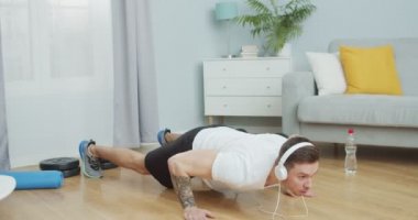 Genç bir Kafkasyalı antrenör kulaklıkla müzik dinleyerek şınav çekiyor. Sporla uğraşan, antrenman yapan ve evde izole edilmiş formda bir sporcu. Sağlıklı ve zengin kavramı.