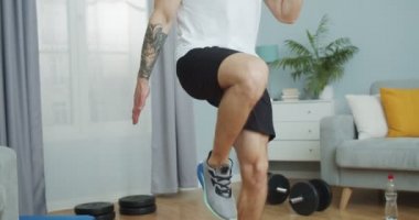 Evde kardiyo kendini izole etme eğitimi alan yakışıklı bir fitness eğitmenini kapat. Beyaz tenli genç bir sporcu bacak egzersizi yapıyor ve diz egzersizleri yapıyor. Sağlık, spor, Wellnes konsepti
