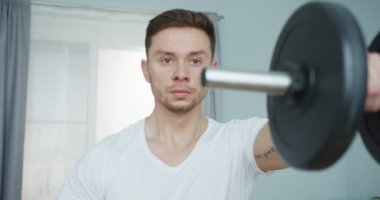 Güçlü atletik adam, sabah egzersizleri yapıyor, evde ısınıyor. Çekici formda erkek, vücudunun üst kısımlarını güçlendirmek için ağırlığını koyuyor. Tecrit döneminde kapalı alanda eğitim.