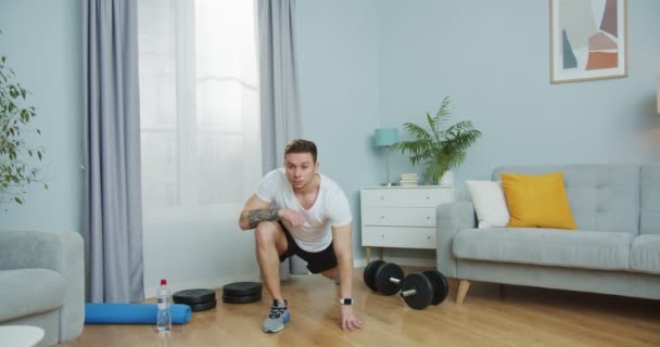 Un tânăr atletic face sport, plămâni pentru a tonifica acasă. Un tip atrăgător care face exerciţii, se linguşeşte, se întinde în sufragerie. Antrenament in usi, antrenament in timpul perioadei de izolare COVID-19 . — Videoclip de stoc