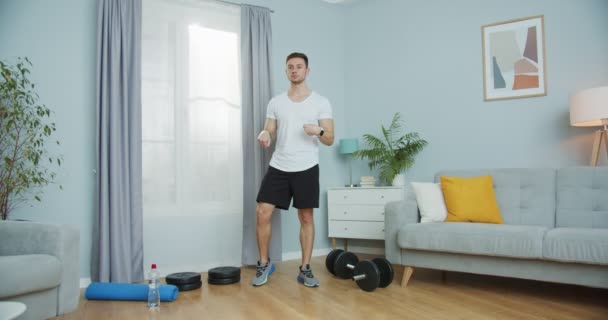Сильний високий чоловік робить ранкове тренування вдома. М'язовий фітнес-інструктор розігрівається, роблячи зап'ястя, вправи на щиколотці перед фізичною активністю. Ізольовані тренування в приміщенні. Спорт, концепція соціальної дистанції . — стокове відео