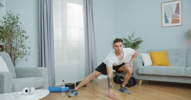 Un jeune homme caucasien qui fait de l'exercice, de la forme physique à la maison. Un homme séduisant qui se réchauffe, qui fait de l'exercice, qui bouge, qui s'étire dans le salon. Concept sportif auto-isolé pendant la pandémie de coronavirus. — Video