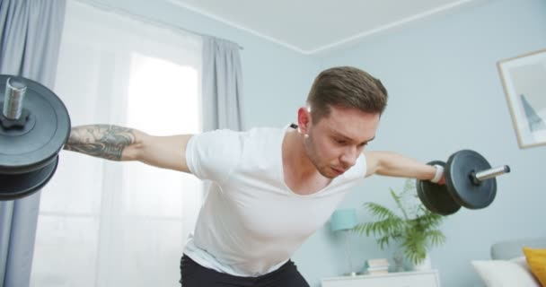 El hombre atlético sudoroso se mantiene en forma, bombeando en casa. Atractivo chico joven deportivo haciendo ejercicios de fila doblado sobre la barra con pesas para fortalecer los músculos. Auto-dedicación, deportes, concepto. — Vídeos de Stock