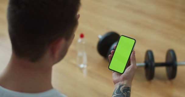 Primer plano caucásico atlético hombre haciendo videollamada en el teléfono inteligente. Fuerte llamada masculina en forma, hablando por teléfono con pantalla verde, tecla de croma, saludando la mano. Autoaislamiento, concepto de comunicación por Internet. — Vídeo de stock