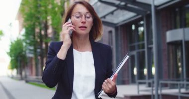 Resmi takım elbiseli çekici beyaz kadın iş bölgesinde sokağa çıkıyor. Gözlüklü, elinde laptop ve kağıtlarla telefonda konuşan güzel bir ofis çalışanı. Çalışma, işgal kavramı.