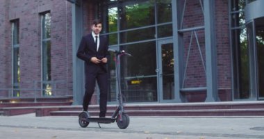 Modern şirket binasının yakınındaki elektrikli tekme scooter 'ına şık bir Kafkas işadamı geliyor. Ata binmek için akıllı telefon kullanan çekici genç bir erkek. Teknoloji, ekoloji kavramı.