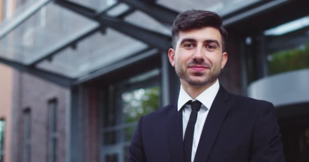 Retrato de atractivo trabajador masculino caucásico en traje formal cerca del edificio de oficinas. Joven empresario inteligente mirando a la cámara y sonriendo al aire libre. Ocupación, profesión, trabajo, espíritu empresarial. — Vídeo de stock