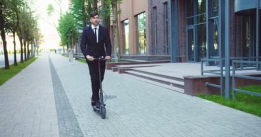 Kendine güvenen yetişkin işadamı, elektrikli scooter nera ofis binalarına biniyor. Çekici beyaz erkek işçi ekolojik nakliye kullanıyor, iş yerine gidiyor. Ulaşım, ekoloji, teknoloji.