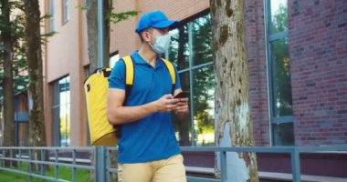 Çekici Kafkasyalı kurye iş bölgesindeki müşterilere sipariş veriyor. Tıbbi maskeli genç bir erkek, adres bulmak için akıllı telefondaki harita uygulamasını kullanıyor. Teslimat servisi, koronavirüs konsepti..