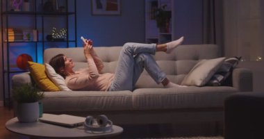 Kafkasyalı güzel bir kadın evinde kanepede dinlenirken ve gülümserken akıllı telefonuna yazıp tıklıyor. Kapalı bir odada uzanıp cep telefonuyla mesajlaşan neşeli bir kadın.