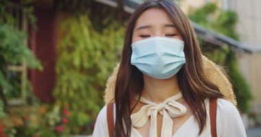 Kapıda durup kameraya bakan, tıbbi maskeli genç Asyalı kadın gezginin portresini yakından çek. Karantinadan sonra kasabada şapkalı güzel bir kadın. Güvenli turizm. Sağlık hizmetleri kavramı