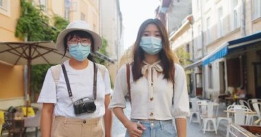 Mutlu anne ve kızın portresi caddede maske takmış ve kameraya iyi bir ruh hali içinde poz veriyor. Fotoğraf makinesi olan güzel bir Asyalı kadın ve şehirde genç bir bayan turist. Seyahat kavramı