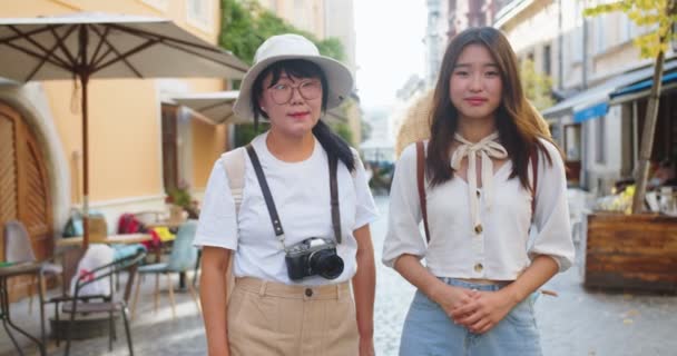 Porträtt av vacker glad asiatisk mor och dotter som står på gatan på gott humör. Ganska glad kvinna i hatt med fotokamera. Ung kvinnlig turist utomhus. Urbana stilar. Turismbegreppet — Stockvideo
