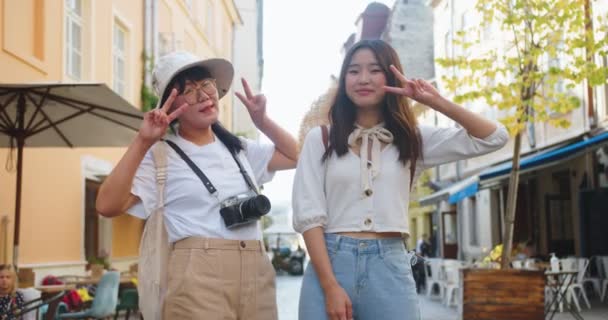 Porträtt av lycklig mor och dotter poserar för kameran på gott humör när du står på gatan utomhus. Vacker rolig asiatisk kvinna i hatt med foto kamera och ung kvinnlig turist. Stadskoncept — Stockvideo