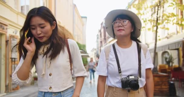 Porträtt av glada mor och dotter resenärer promenader tillsammans. Ung asiatisk kvinnlig turist talar på mobiltelefon i staden. Vacker kvinna ringer på smartphone och visar något för mamma — Stockvideo