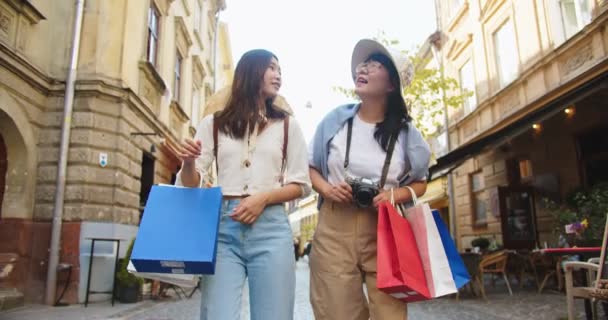 Smukke glade asiatiske kvinder taler, mens du går udendørs i gamle bydel med indkøbsposer. Glædelig ung kvindelig turist viser mor køb. Kvinde med overrasket ansigt. Indkøbskoncept – Stock-video