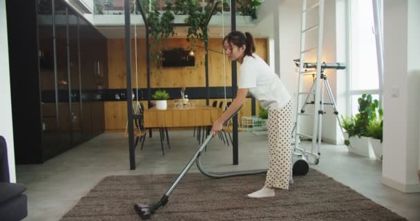 Szczęśliwy wesoły młody piękny azjatycki kobieta za pomocą nowoczesnego odkurzacza podłogi dywan w jasny przytulny salon w domu. Koncepcja sprzątania, sprzątania, stylu życia. — Wideo stockowe
