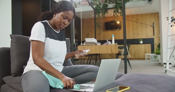 Närbild av afrikansk amerikansk kvinna besprutning antiseptisk, rengöring laptop tangentbord med desinfektionsmedel våt torka sitter på soffan. Begreppet hushållning, desinfektion, skydd, förebyggande, coronavirus. — Stockvideo