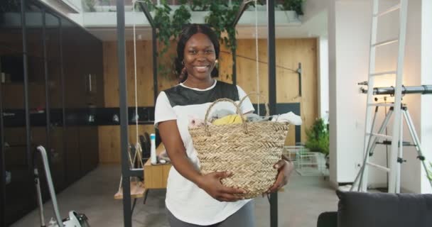 Primer plano de feliz alegre joven hermosa mujer afroamericana sosteniendo cesta con ropa sucia, servicio de lavandería. Concepto de limpieza, casa de limpieza familiar, estilo de vida. — Vídeos de Stock